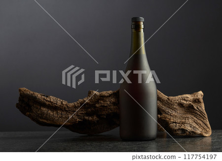 Bottle of brandy and old snag on a black background. 117754197