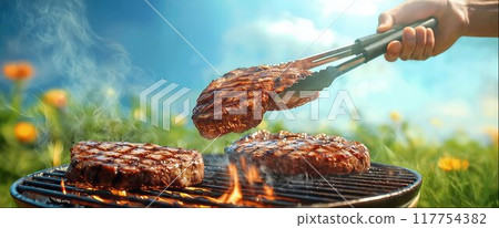 Chef holding large steak with meat tongs over flaming grill, close-up, copy space Chef holding large steak with meat tongs over flaming grill, close-up, copy space 117754382