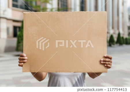 Unidentified person holding a blank cardboard sign mock up in an urban setting 117754413