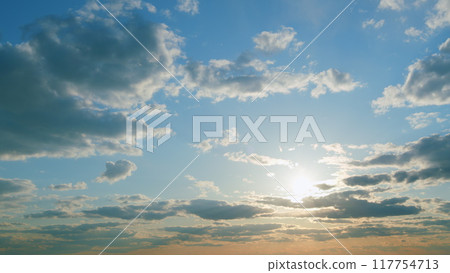 Sun below the horizon and clouds in the fiery dramatic sky. Clouds illuminated by sunbeams. Timelapse. 117754713