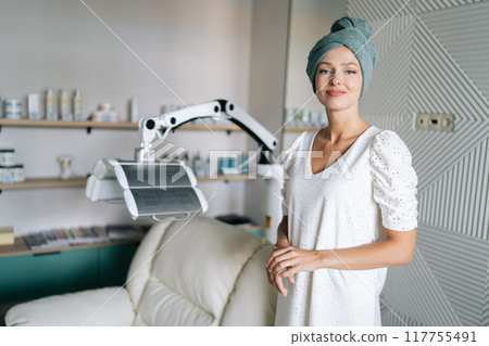Portrait of cute young woman with blonde hair in spa towel standing posing looking at camera after washing hair in beauty salon with casual and relaxed atmosphere. Beauty and hair styling concept 117755491