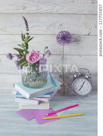 A stack of books, an alarm clock, a bouquet of flowers and stationery materials on a wooden background. Back to school. A stack of books, an alarm clock, a bouquet of flowers and stationery materials on a wooden background. Back to school. 117755857