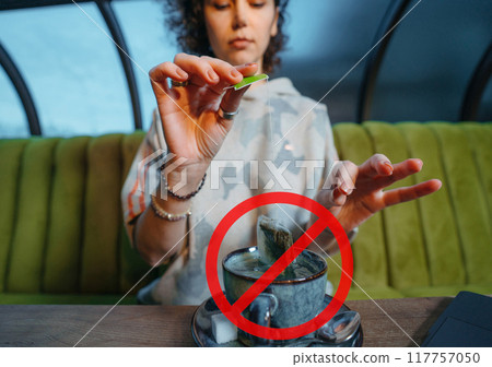 Woman brewing a fresh mug of tea with teabag in a cafe with crossed out stop sign Woman brewing a fresh mug of tea with teabag in a cafe with crossed out stop sign 117757050