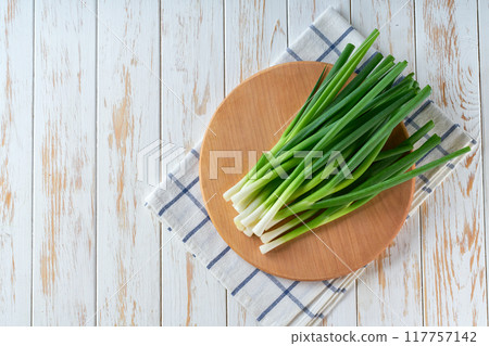 young green onions or scallions on a cutting board on white wooden table, copy space for text. young green onions or scallions on a cutting board on white wooden table, copy space for text. 117757142