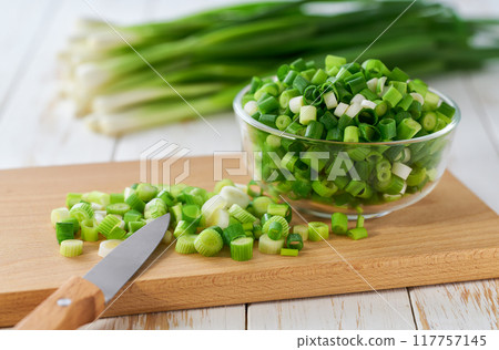 Chopped fresh green onion or scallions in a clear glass bowl , on a white table. 117757145