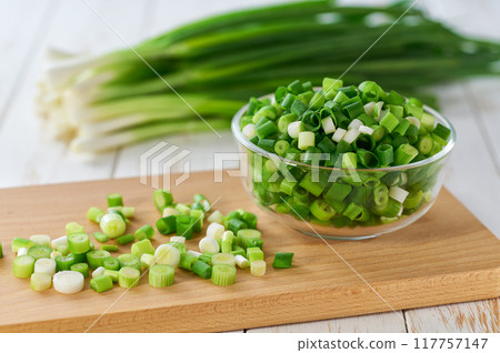 Chopped scallions or young spring onion in a clear glass , on a kitchen table. Chopped scallions or young spring onion in a clear glass , on a kitchen table. 117757147