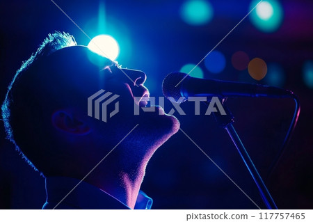 A silhouette of a singer performing on stage, illuminated by a bright spotlight, with colorful bokeh lights in the background A silhouette of a singer performing on stage, illuminated by a bright spotlight, with colorful bokeh lights in the background 117757465