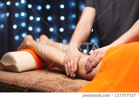 Massage therapist massaging calf muscles of woman in spa center, side view. Close-up of hands of wellness and body care specialist 117757537
