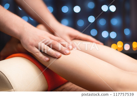 Massage therapist massaging calf muscles of woman in spa center, side view. Close-up of hands of wellness and body care specialist Massage therapist massaging calf muscles of woman in spa center, side view. Close-up of hands of wellness and body care specialist 117757539