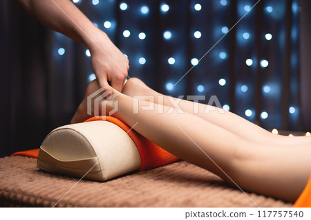 Massage therapist massaging calf muscles of woman in spa center, side view. Close-up of hands of wellness and body care specialist 117757540