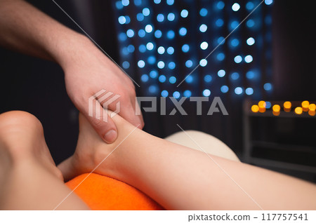 Massage therapist massaging calf muscles of woman in spa center, side view. Close-up of hands of wellness and body care specialist Massage therapist massaging calf muscles of woman in spa center, side view. Close-up of hands of wellness and body care specialist 117757541