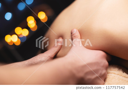Woman receiving neck massage in beauty salon. Unrecognizable girl lies face down on massage table in semi-darkness 117757542