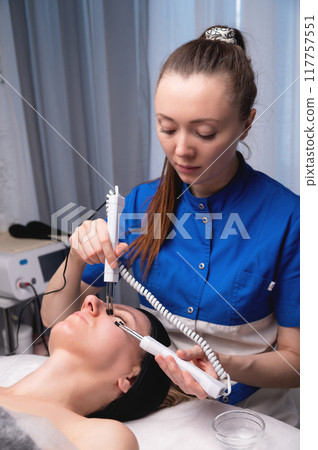 Ultrasonic facial treatment on ultrasound face machine. Woman taking electric lift massage spa salon. Stimulation muscles on professional equipment microcurrent therapy. New methods of rejuvenation Ultrasonic facial treatment on ultrasound face machine. Woman taking electric lift massage spa salon. Stimulation muscles on professional equipment microcurrent therapy. New methods of rejuvenation 117757551