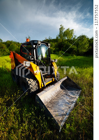 Small bulldozer will level the ground, preparing for new housing construction. Construction equipment on green grass in a field 117757552
