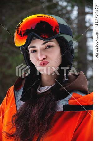 female skier or snowboarder standing and making funny faces at the camera in ski clothes and gear. extreme winter sport at the resort 117757557