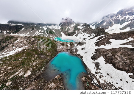 Aerial wide angle view of an alpine lake high in the mountains. Lake surrounded by mountain peaks partially covered with snow 117757558