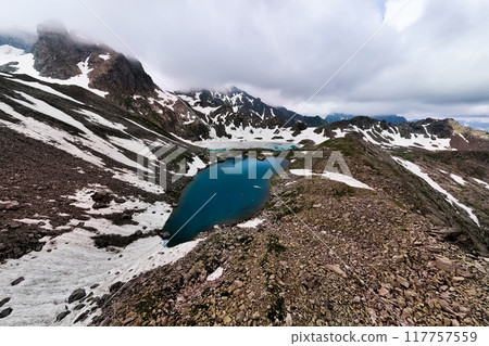 Stunning aerial view of the lake and surrounding mountains covered in snow on a beautiful summer day. Panoramic views of the peaks and the beauty of untouched nature 117757559
