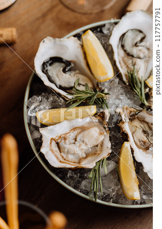 Fresh oysters on ice served with lemon wedges and rosemary, perfect for gourmet seafood lovers Fresh oysters on ice served with lemon wedges and rosemary, perfect for gourmet seafood lovers 117757791