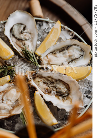 Fresh oysters on ice served with lemon wedges and rosemary, perfect for gourmet seafood lovers 117757795