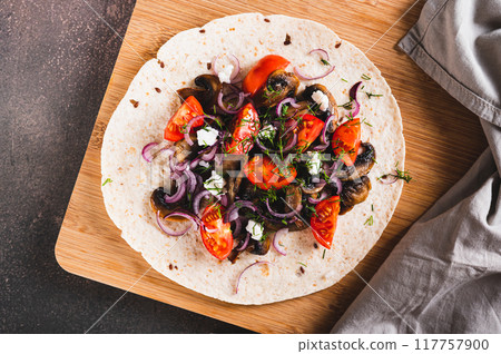 Close up of tacos with fried mushrooms, tomatoes, onions and feta on a board top view Close up of tacos with fried mushrooms, tomatoes, onions and feta on a board top view 117757900
