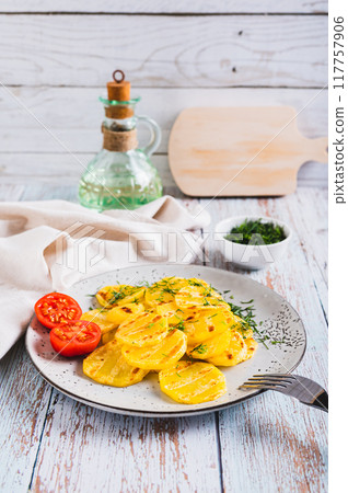 Appetizing grilled potatoes with tomatoes and dill on a plate on the table vertical view 117757906
