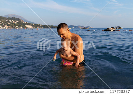 A father tenderly bathes his two-year-old daughter in the sea. A father tenderly bathes his two-year-old daughter in the sea. 117758287