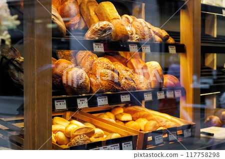 German bakery counter showcase display with many different baked bread price tags and names.  Fresh hot crusty pastry product assortment variety at european retail grocery store market 117758298