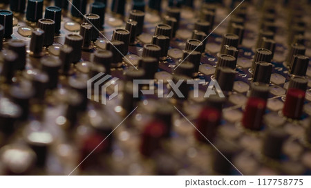 Pre amp knobs and switchers on mixing console panel board, audio stereo equipment used in music post production. Empty control room in professional studio, fader and sliders. Close up. 117758775