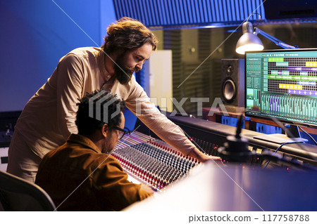Diverse team of artist and audio engineer composing a hit song, working in professional music studio with technical gear. Musician with expert editing and recording music on mixing console board. 117758788