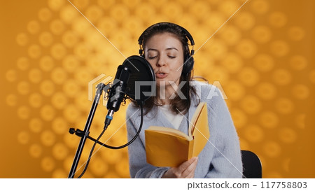 Voice actor reading book, recording for audiobook production using microphone and headset, studio background. Person using mic and headphones to produce digital recording of novel, camera B 117758803