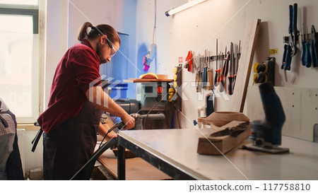 Carpenter collaborating with apprentice, using orbital sander with fine sandpaper to achieve refined finish. Manufacturer and BIPOC colleague using angle grinder on wood block, camera B Carpenter collaborating with apprentice, using orbital sander with fine sandpaper to achieve refined finish. Manufacturer and BIPOC colleague using angle grinder on wood block, camera B 117758810