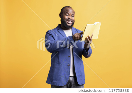 Cheerful man reading interesting book, pointing finger to favorite part on page. Joyous person having fun enjoying literature novel during leisure time, isolated over studio background Cheerful man reading interesting book, pointing finger to favorite part on page. Joyous person having fun enjoying literature novel during leisure time, isolated over studio background 117758888