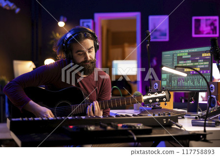 Producer composing music with his acoustic guitar in home studio, recording acoustical tunes on strings and singing melody. Audio engineer mixing and mastering his song with production gear. Producer composing music with his acoustic guitar in home studio, recording acoustical tunes on strings and singing melody. Audio engineer mixing and mastering his song with production gear. 117758893