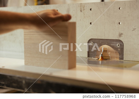 Man putting lumber block through spindle moulder, creating smooth and precise edges on wooden pieces. Joiner using heavy machinery to craft strong and seamless joints for furniture and structures Man putting lumber block through spindle moulder, creating smooth and precise edges on wooden pieces. Joiner using heavy machinery to craft strong and seamless joints for furniture and structures 117758968