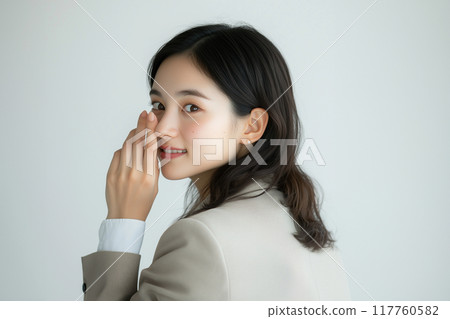 Whispering. Asian woman in her 20s posing to whisper. White background. Beige suit. 117760582