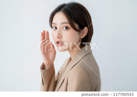 Whispering. Asian woman in her 20s posing to whisper. White background. Beige suit. Whispering. Asian woman in her 20s posing to whisper. White background. Beige suit. 117760583
