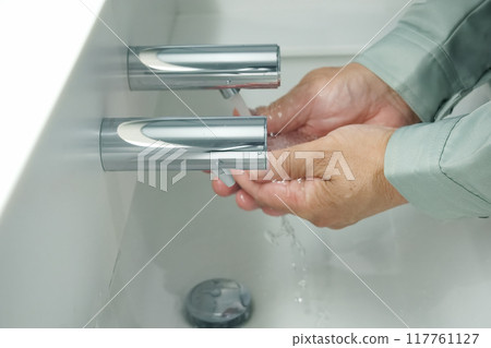 A man in work clothes washing his hands A man in work clothes washing his hands 117761127
