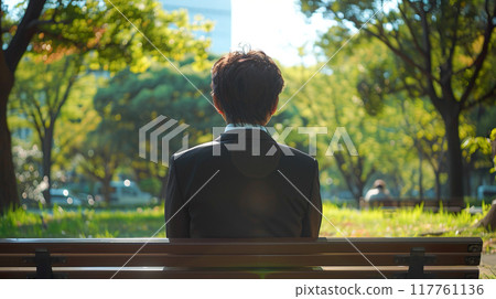 一個穿著西裝的男人坐在公園長椅上的後面視圖 117761136