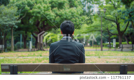 一個穿著西裝的男人坐在公園長椅上的後面視圖 117761137