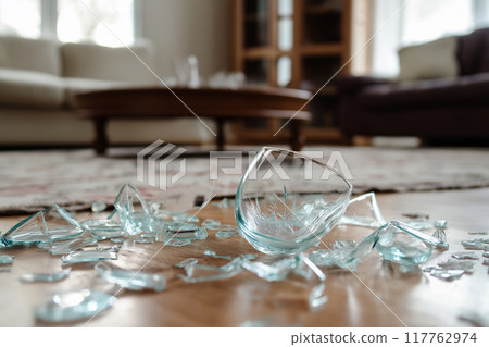 Pieces of glass cup broken on wooden floor. Earthquake damage. 117762974