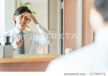 A young Asian businessman in a suit taking his temperature in the bathroom (fever, fever, cold, infection prevention) A young Asian businessman in a suit taking his temperature in the bathroom (fever, fever, cold, infection prevention) 117763573
