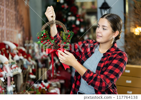 Joyful woman in shirt checking the material of a small space Christmas viburnum wreath before New Year in a shopping mall 117764138