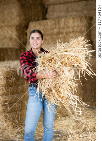Portrait of positive female farmer with straw in her hands in an animal feed warehouse Portrait of positive female farmer with straw in her hands in an animal feed warehouse 117764157