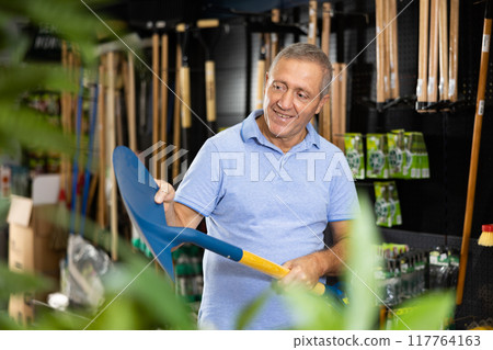 Attentive middle-aged male consumer choosing a new shovel for gardening in a hardware store 117764163