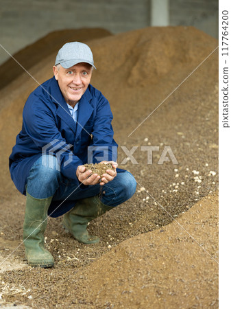 Smiling dairy farm male worker holding rapeseed animal feed 117764200