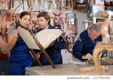 Portrait of three woodworkers restorers renovating Victorian chair and mirror frame in workshop 117764305