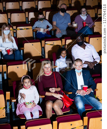 Adults with children in protective masks watching movie in cinema Adults with children in protective masks watching movie in cinema 117764318