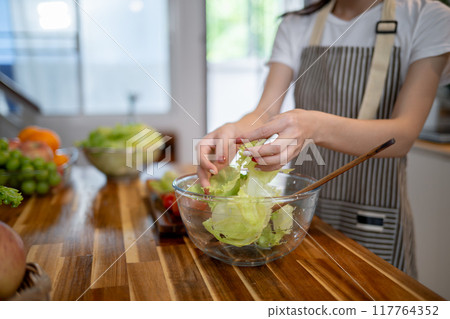 A close-up image of a woman preparing a salad bowl at the kitchen table, making healthy food at home A close-up image of a woman preparing a salad bowl at the kitchen table, making healthy food at home 117764352