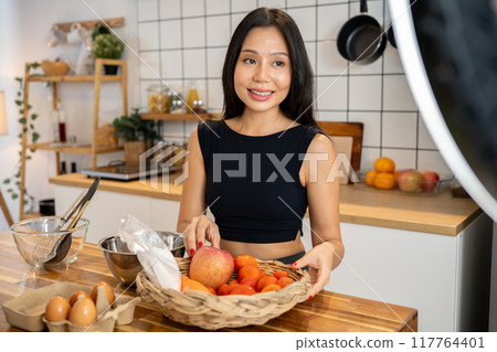 An attractive Asian female food blogger is cooking in front of the camera, recording a video. 117764401