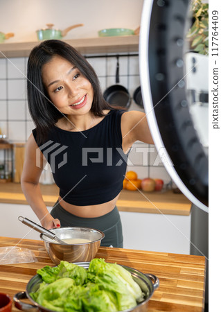 Beautiful Asian female food blogger is recording herself while making a healthy dish in the kitchen. 117764409